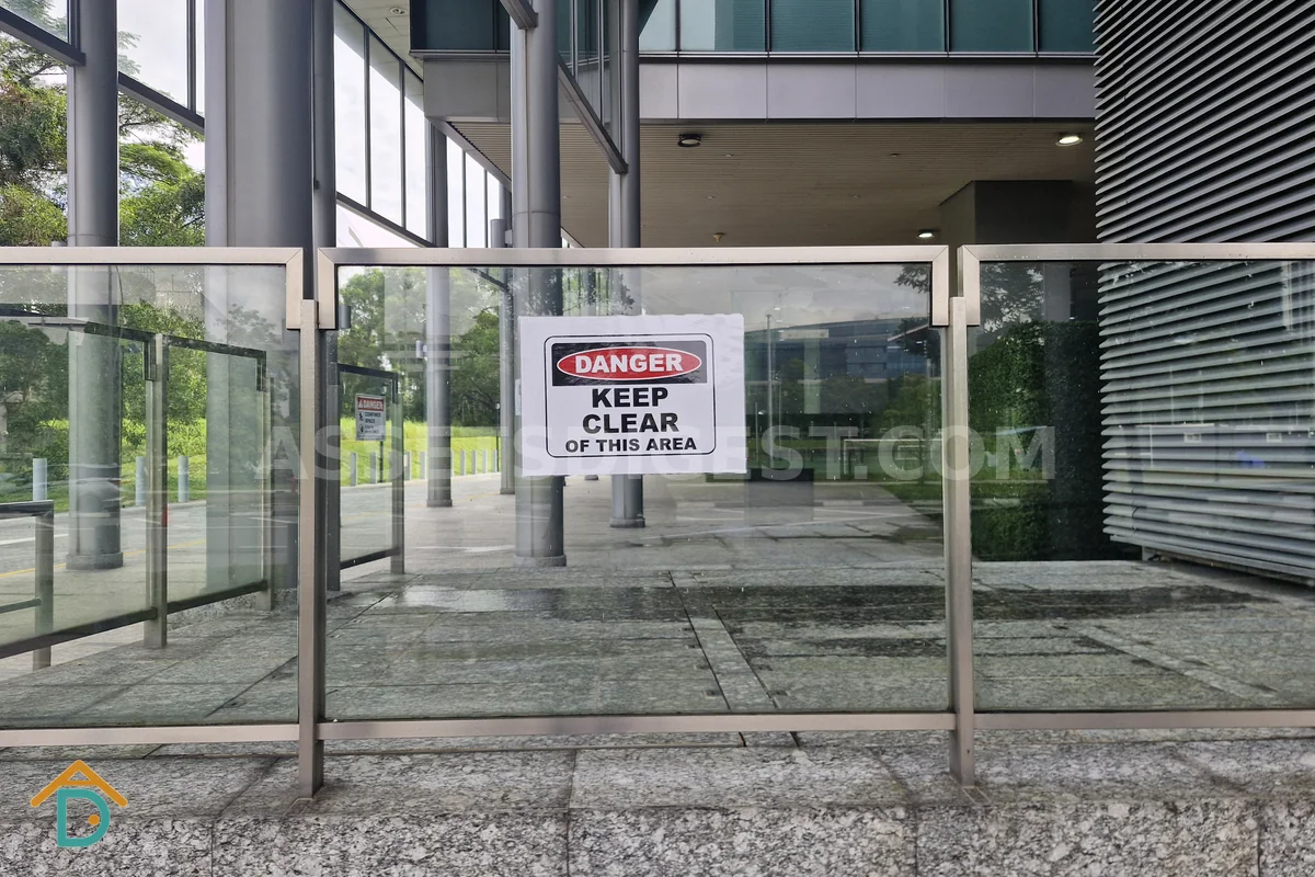 Red-and-white danger sign reading 'Keep Clear of This Area' fixed to a glass panel outside a building lobby