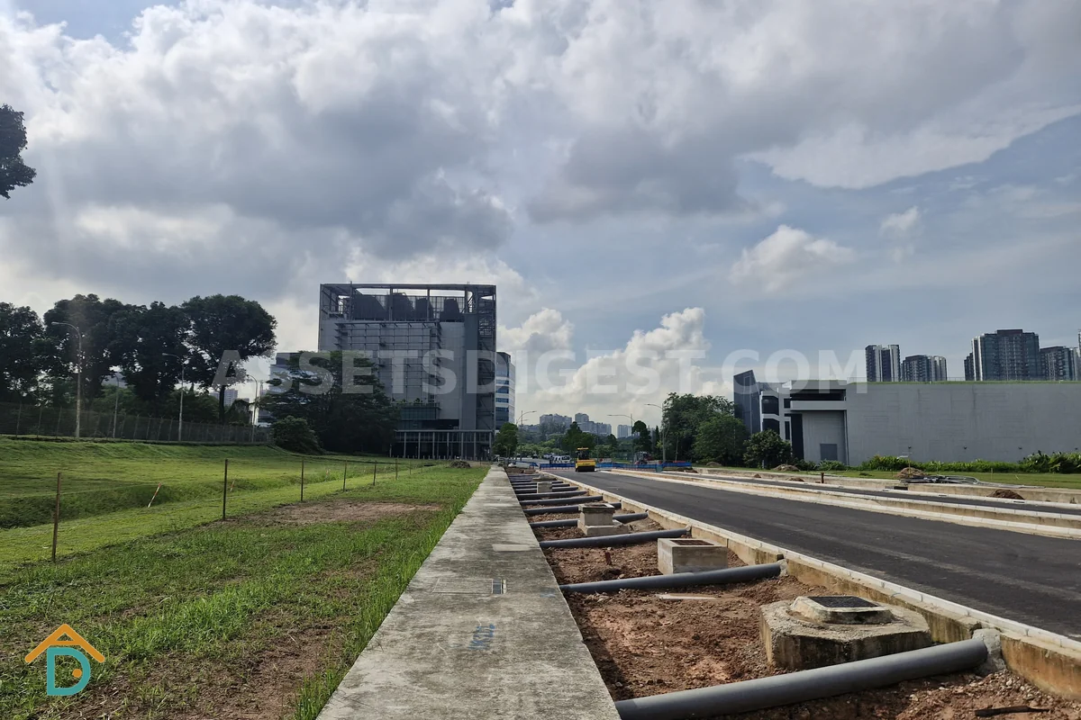 Partially built steel-frame structure beside a freshly laid road, with high-rise residential blocks in the background