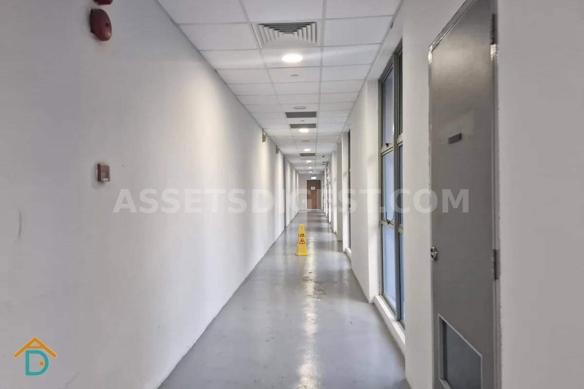 Empty corridor lined with unit doors, a yellow wet-floor caution cone standing in the middle of the walkway