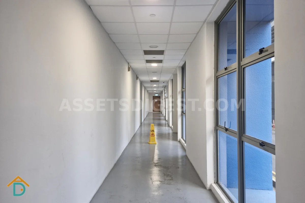 Empty corridor lined with unit doors, a yellow wet-floor caution cone standing in the middle of the walkway